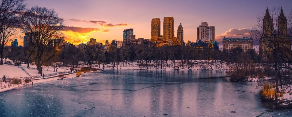 Festive, snowy Central Park with frozen lake at sunset